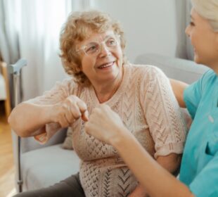 Happy senior woman doing fist bump with nurse at home